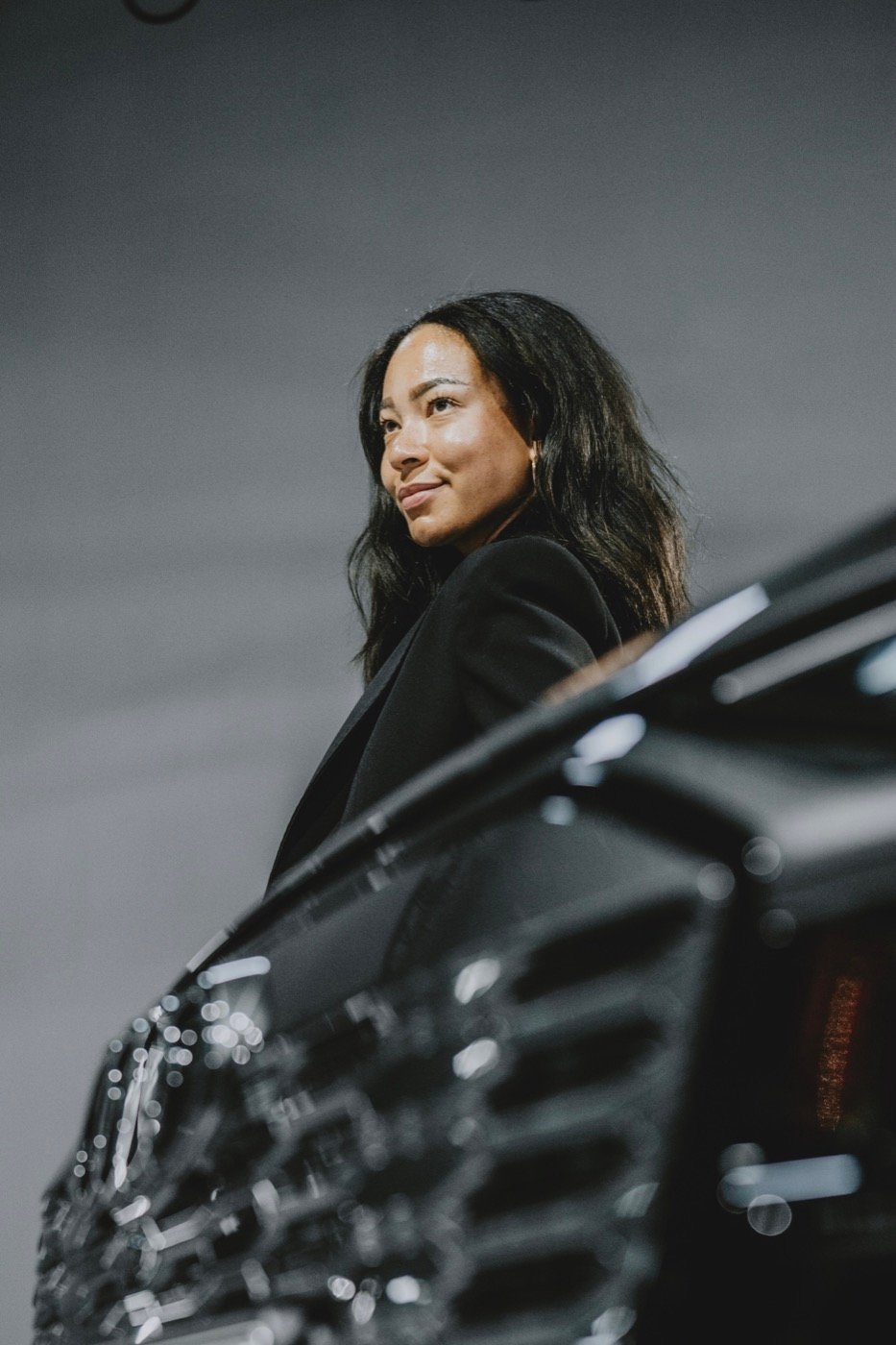 Founder in a black jacket standing beside a car in a dark studio